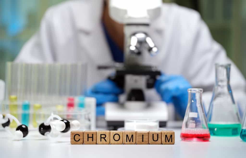Pesquisador olhando, ao fundo, em um microscópio; à frente, pequenos blocos mostram a palavra "chromium"