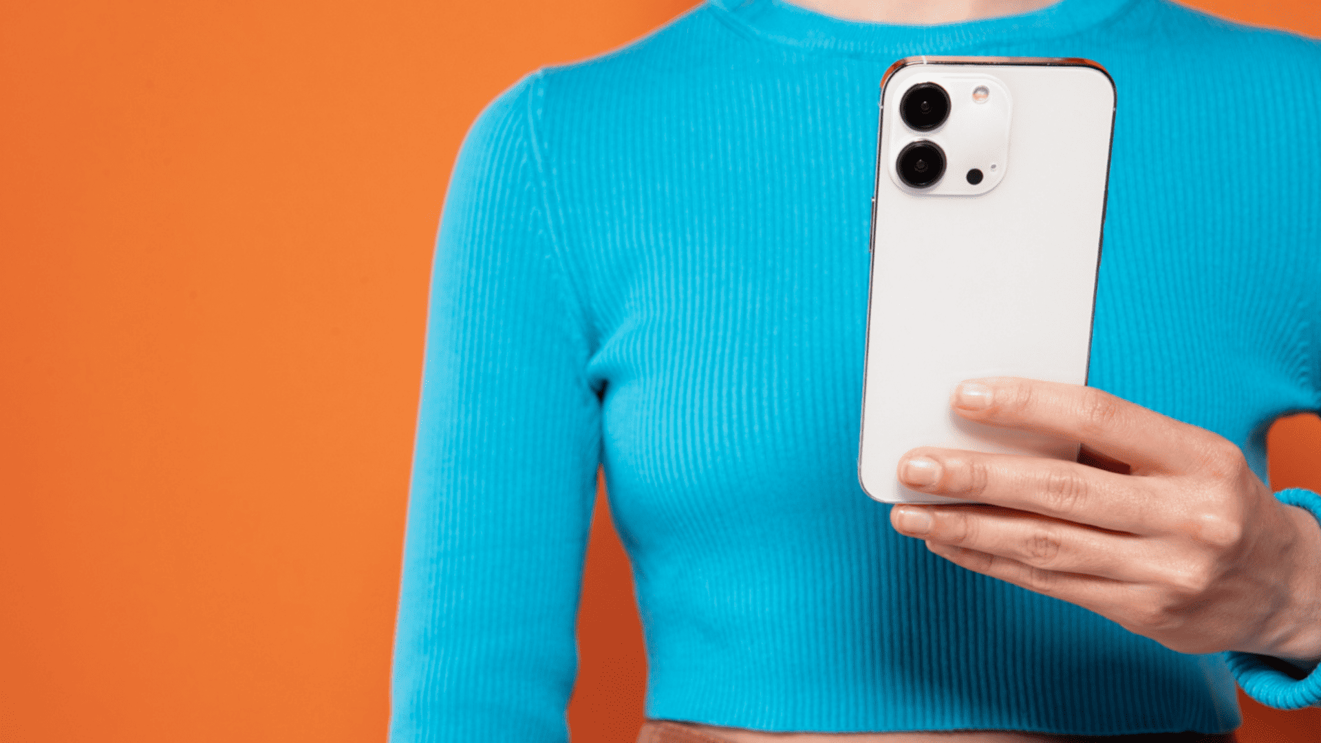 mulher segurando iphone com uma blusa azul e fundo laranja