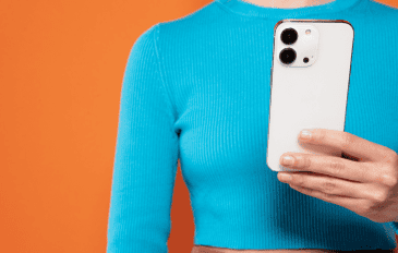 mulher segurando iphone com uma blusa azul e fundo laranja