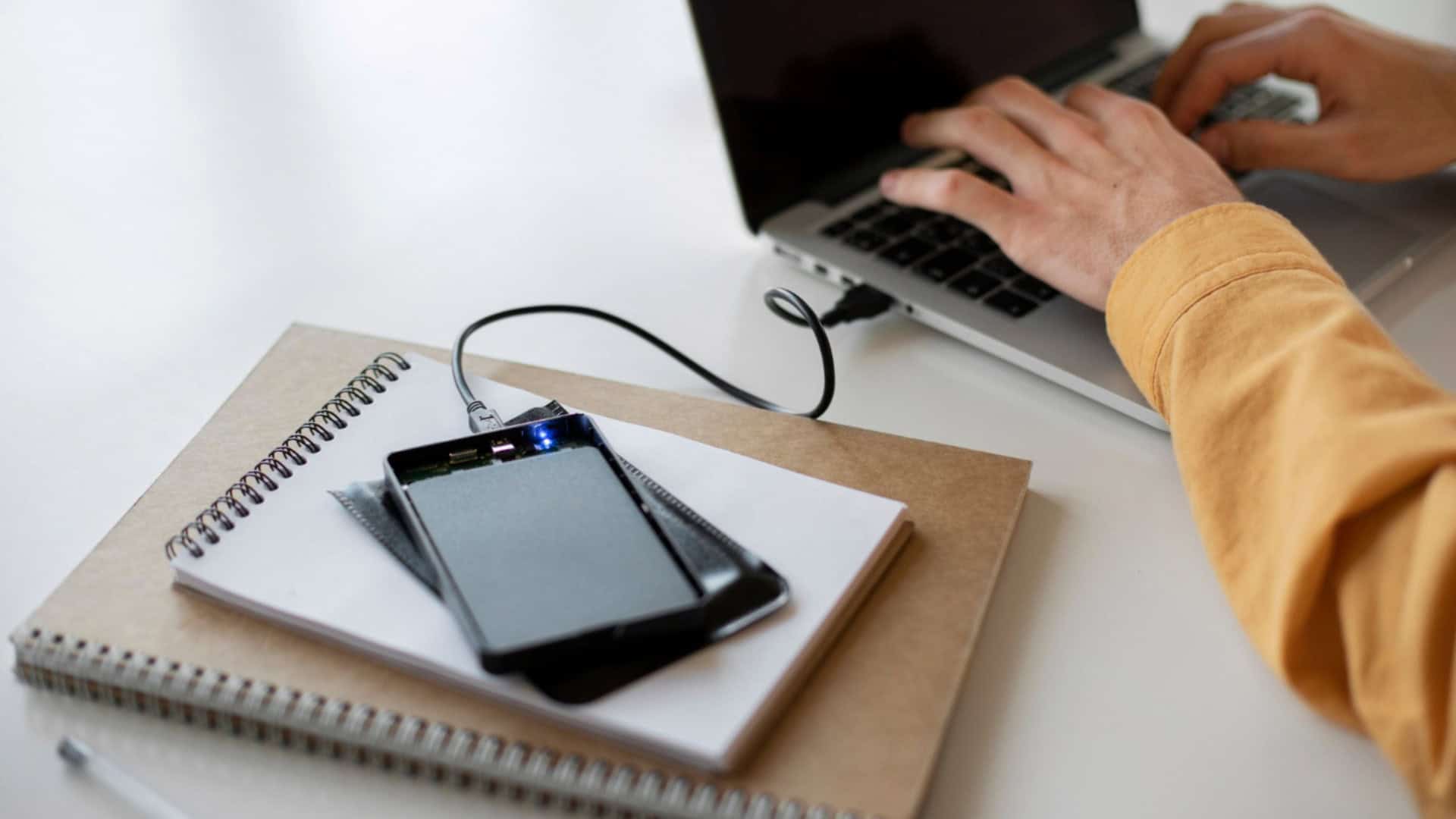 pessoa usando o notebook com um ssd externo conectado