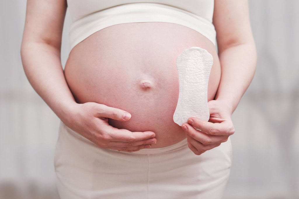 Uma mulher grávida segura um absorvente higiênico nas mãos