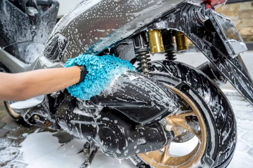 Imagem mostra pessoa lavando a mão a motocicleta com espuma de limpeza