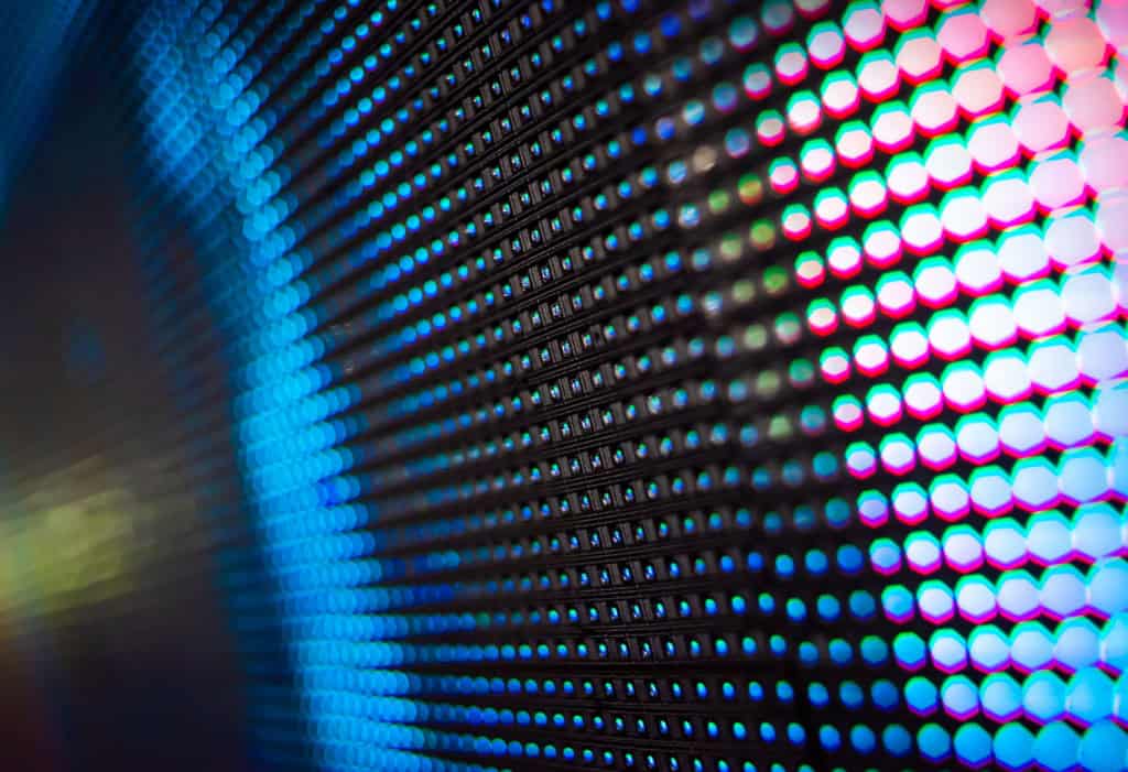 Imagem mostra grandes telas de projeção LED em fundo abstrato colorido.