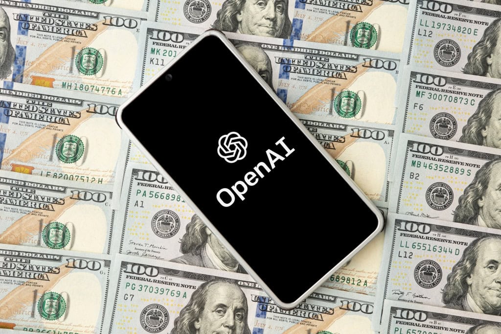 Logo da OpenAI em smartphone que está em cima de notas de dólar