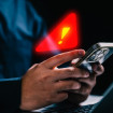 Pessoa usando iPhone com símbolo de alerta de segurança em cima do celular