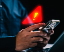 Pessoa usando iPhone com símbolo de alerta de segurança em cima do celular