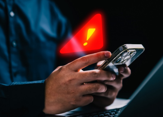 Pessoa usando iPhone com símbolo de alerta de segurança em cima do celular
