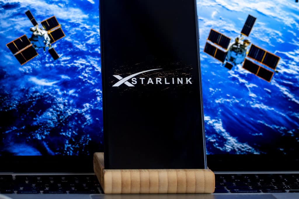 Logo da Starlink em um smartphone com satélites ao fundo