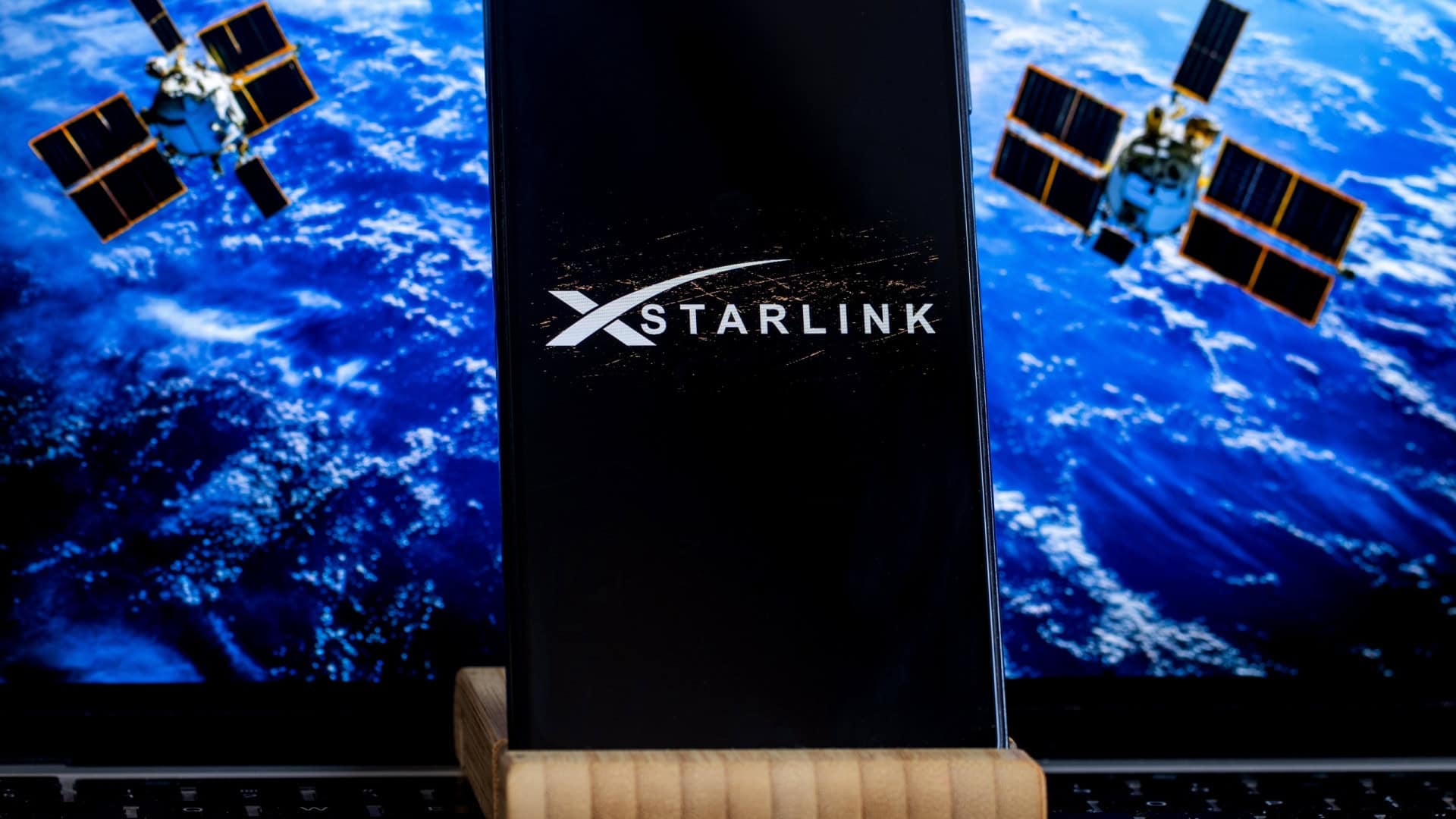 Logo da Starlink em um smartphone com satélites ao fundo
