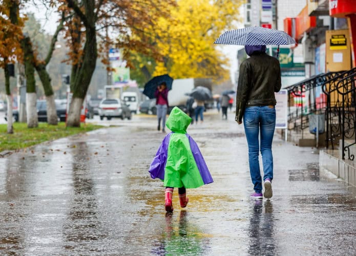 Mulher e criança de costas andando na chuva; a mulher está segurando um guarda-chuva