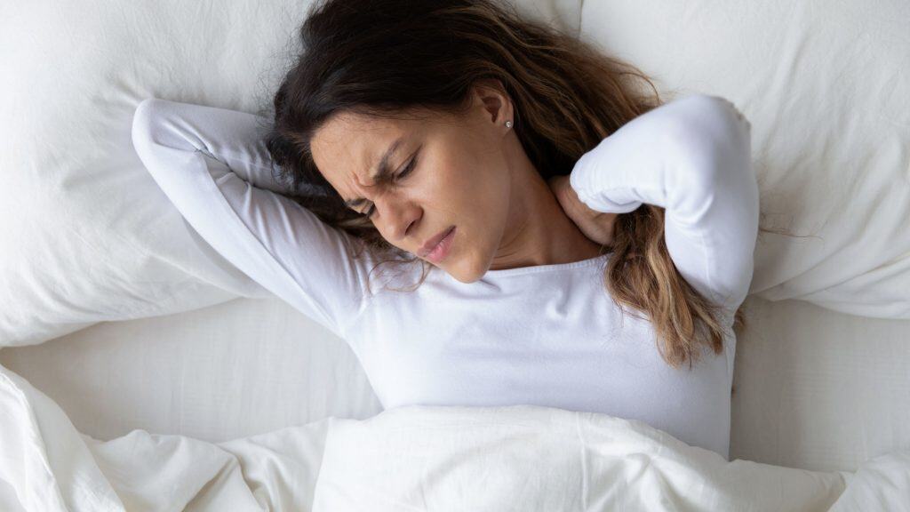 Mulher jovem sentindo dor no pescoço ao acordar 