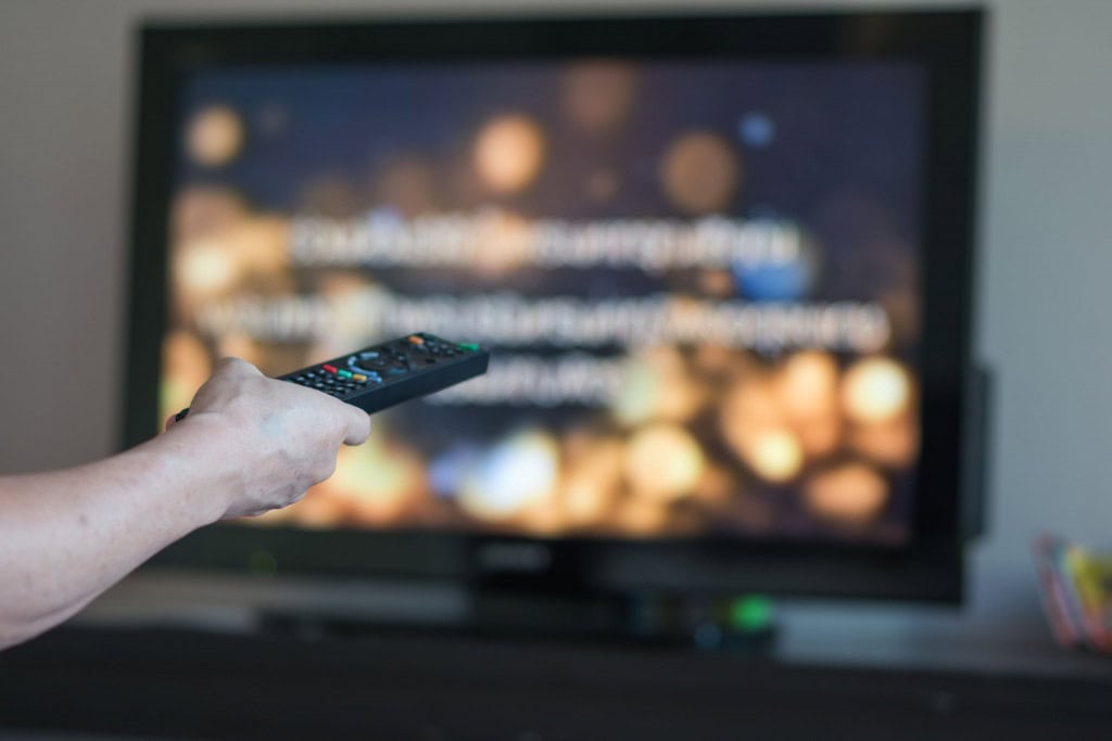 Imagem ilustrativa de uma mão segurando um controle remoto apontando para a tela da TV