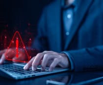 Pessoa digitando em um teclado de notebook com um sinal de alerta pairando sobre o teclado