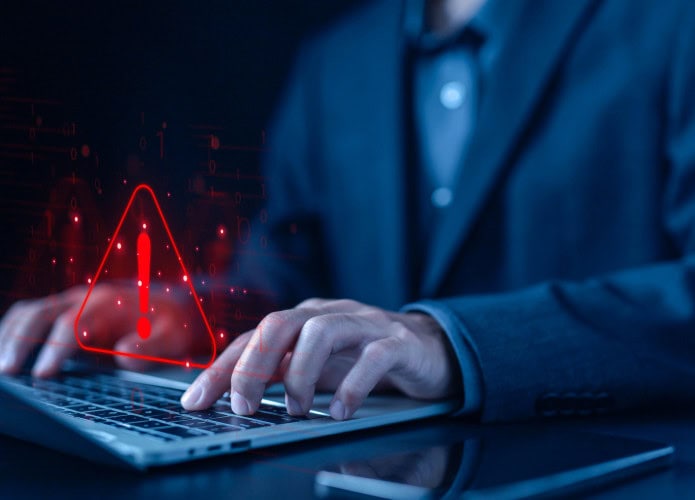 Pessoa digitando em um teclado de notebook com um sinal de alerta pairando sobre o teclado