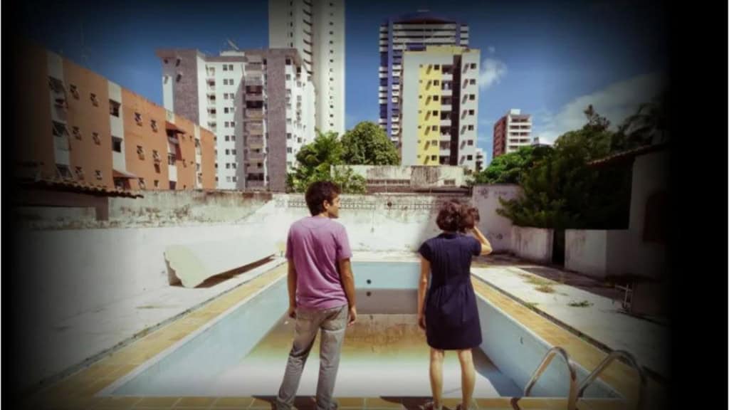 uma mulher e um homem estão conversando em frente a uma piscina vazia