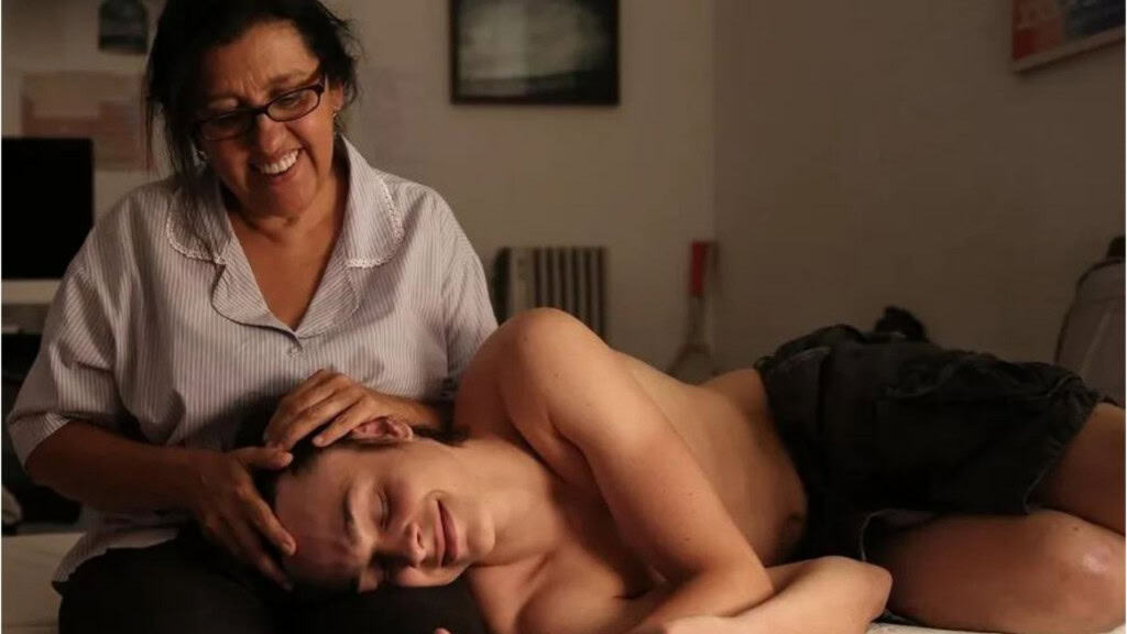 Mulher sorrindo com jovem deitado em seu colo, ela faz carícias no cabelo dele.