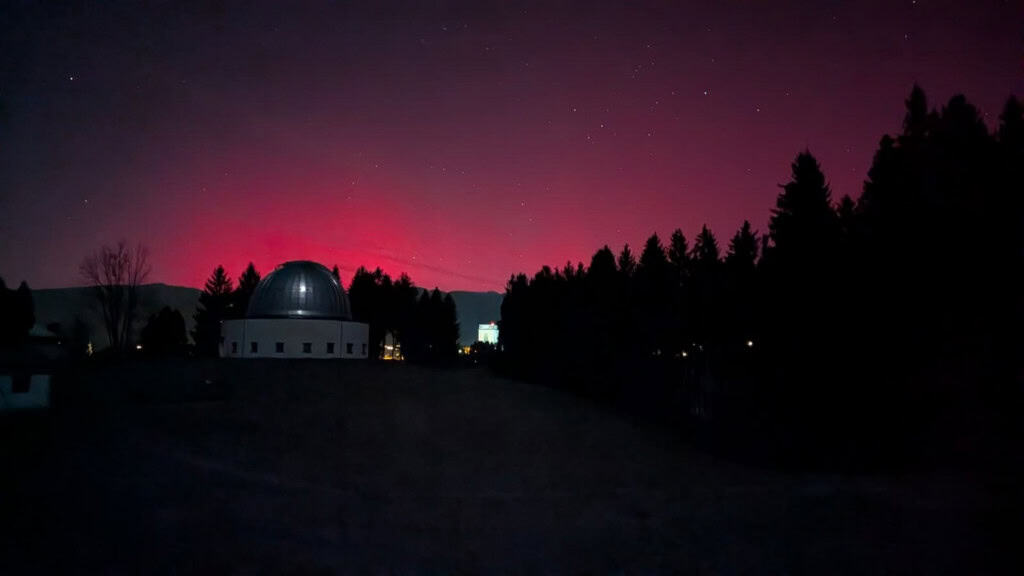 Céu noturno com aurora avermelhada no horizonte marcando silhueta de observatório na Itália