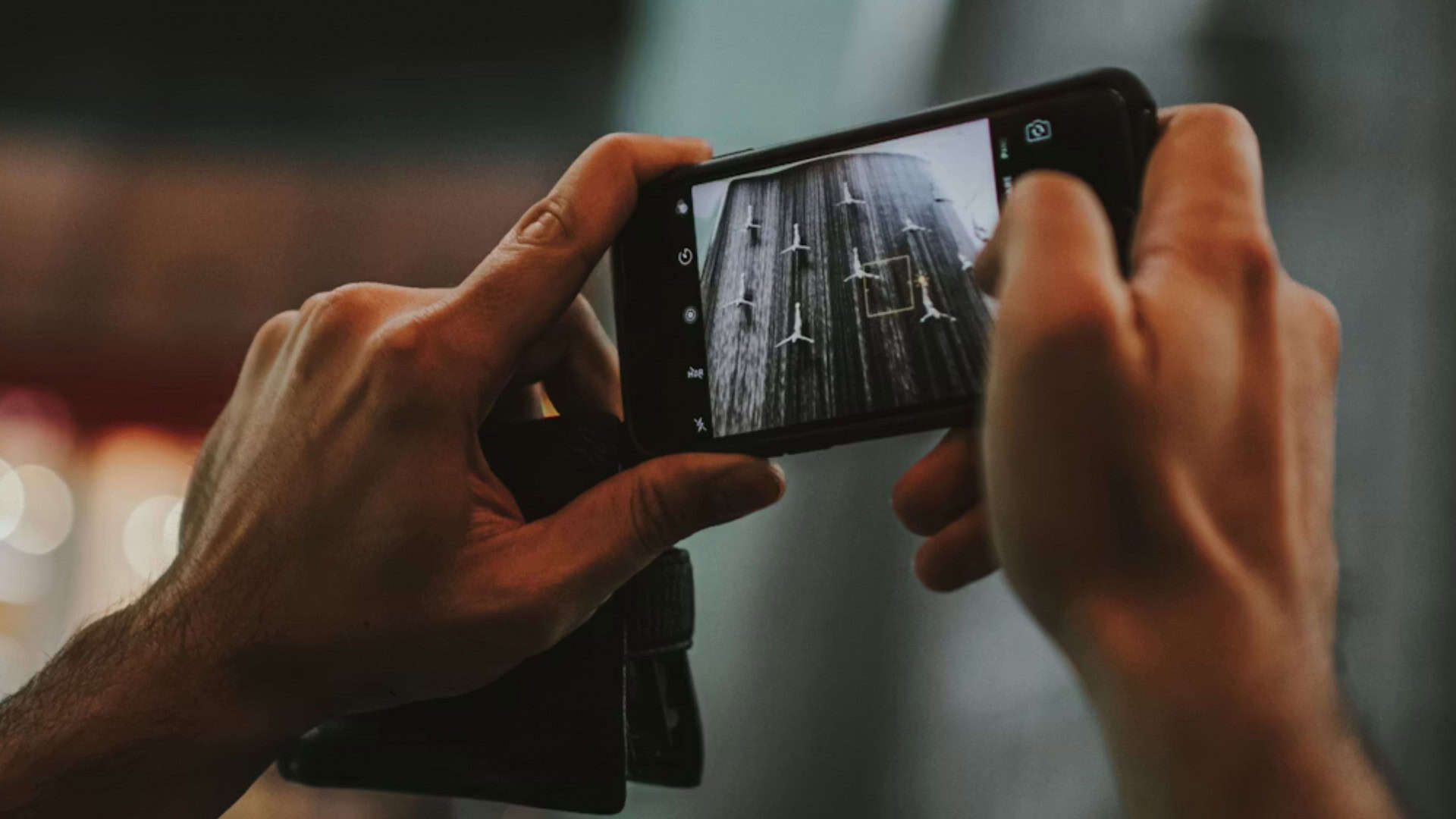 Pessoa segurando o celular com duas mãos, a tela mostra que a câmera está ligada, apontando para um quadro em preto e branco.