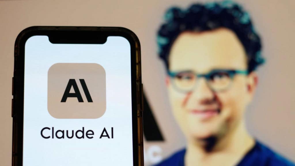 Ao fundo, Dario Amodei, cuja imagem está borrada; à frente, logo do Claude AI em um smartphone