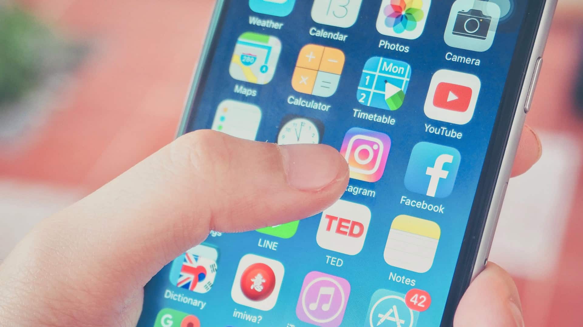 Pessoa está prestes a tocar o ícone do Instagram na tela do celular, cercado por outros aplicativos organizados em grade.