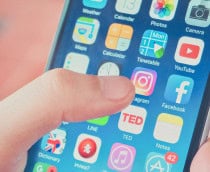 Pessoa está prestes a tocar o ícone do Instagram na tela do celular, cercado por outros aplicativos organizados em grade.