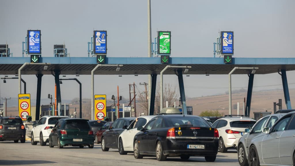 Cabines de pedágio em área rural com várias faixas abertas, carros alinhados e placas indicando pagamento em dinheiro ou cartão.