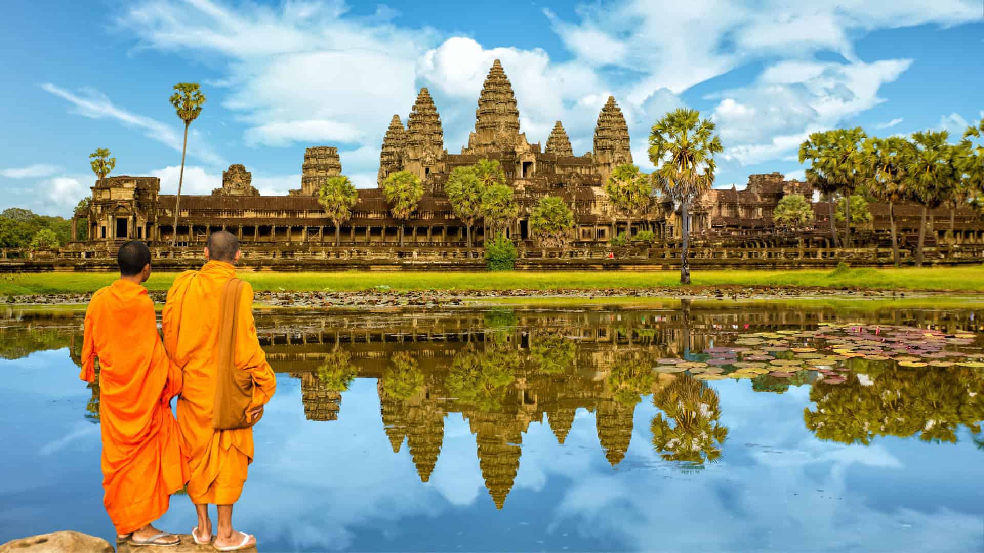 Dois monges em beira de espelho d'água olhando para templo Angkor