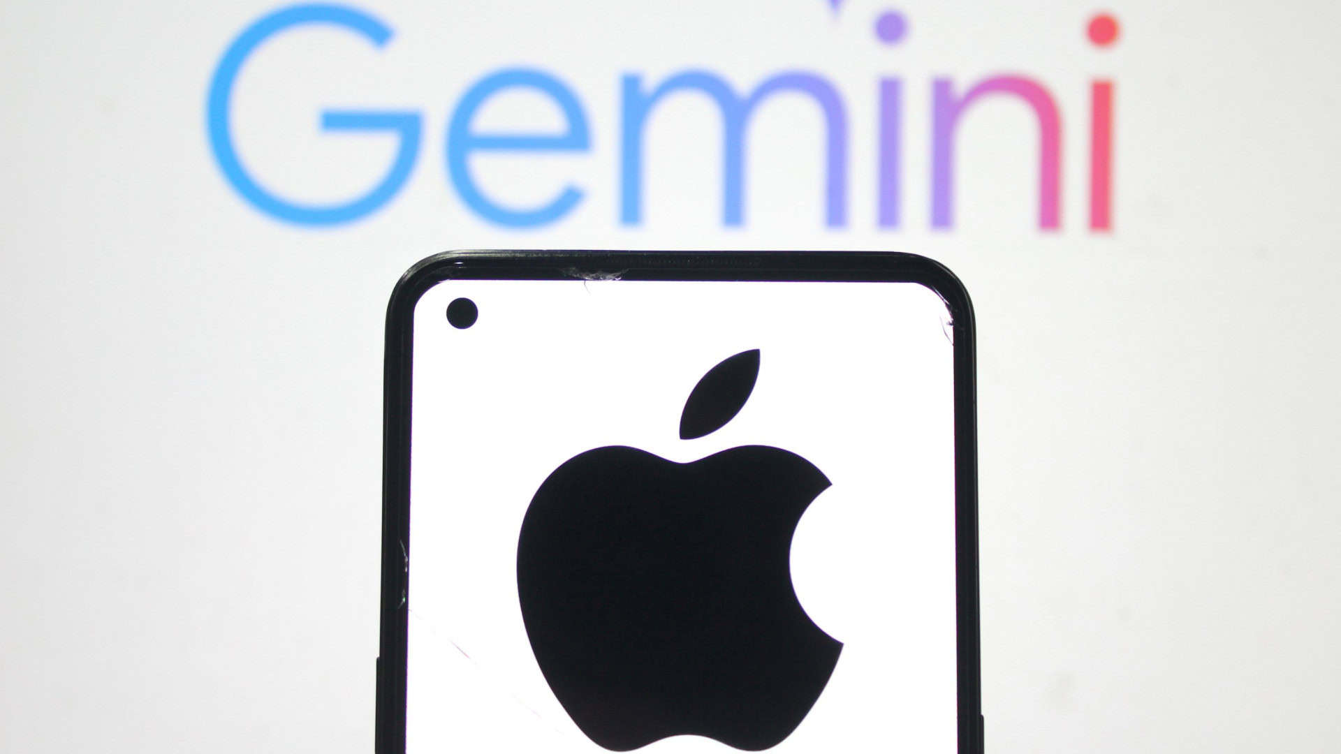 Celular exibindo logomarca da Apple na tela colocado na frente de outra tela exibindo logomarca do Gemini, do Google