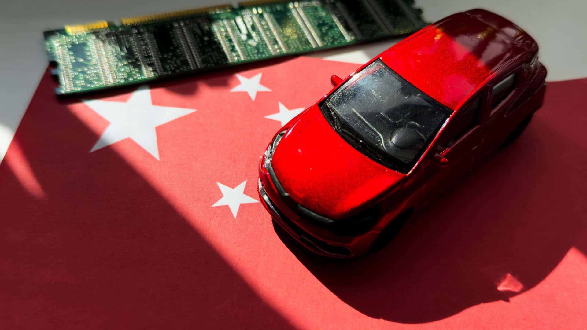 Miniatura de carro em cima de miniatura de bandeira da China; ambos estão ao lado de um chip