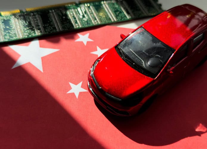 Miniatura de carro em cima de miniatura de bandeira da China; ambos estão ao lado de um chip