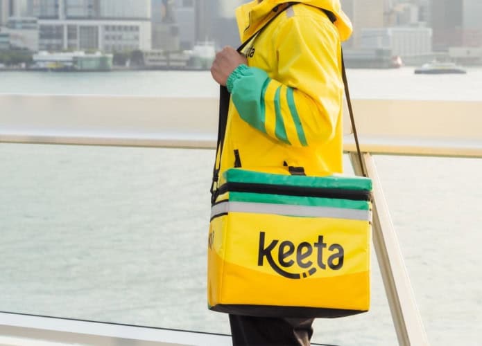 Homem em pé com uniforme e bolsa da Keeta