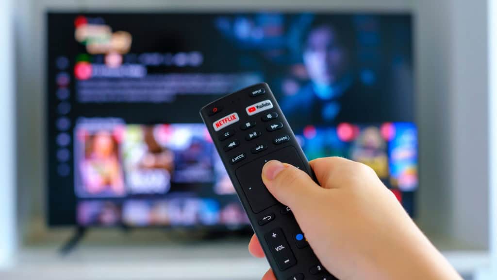 Pessoa segurando controle de TV com botões da Netflix e do YouTube