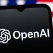 Celular com logotipo da OpenAI na tela colocado na frente de tela exibindo bandeira dos Estados Unidos