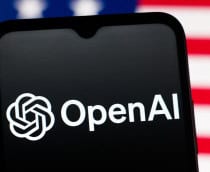 Celular com logotipo da OpenAI na tela colocado na frente de tela exibindo bandeira dos Estados Unidos