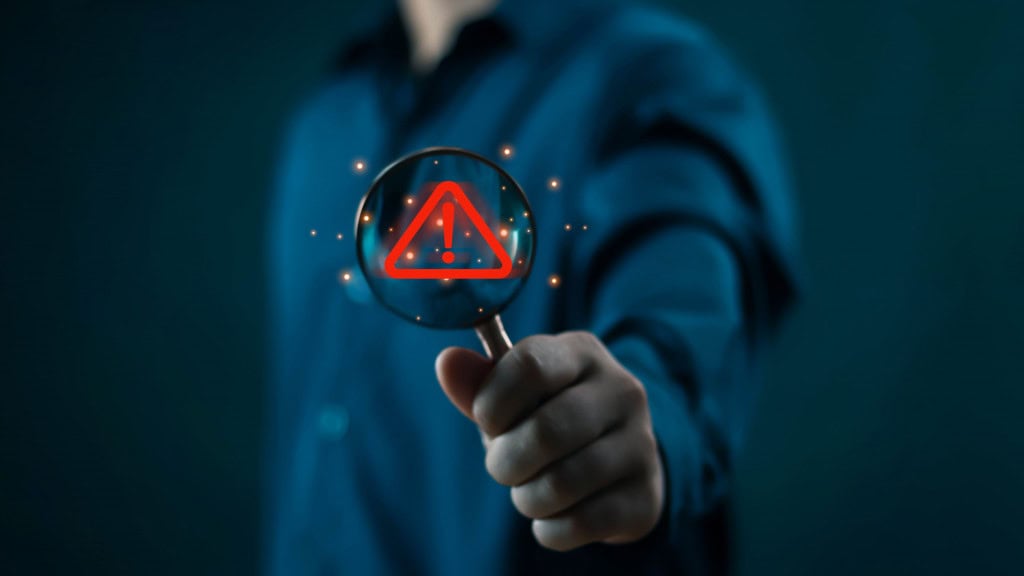 Montagem de homem segurando lupa com símbolo de perigo no vidro