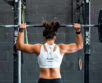 Mulher de costas, em frente a um apralho de academia, fazendo levantamento de peso.