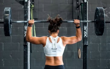 Mulher de costas, em frente a um apralho de academia, fazendo levantamento de peso.