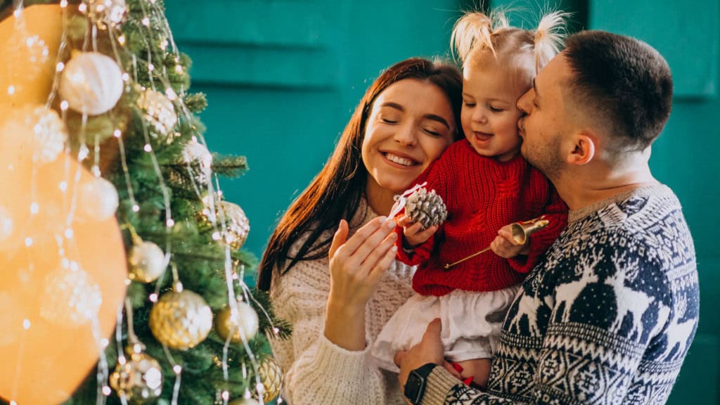 Família com filha pendura brinquedos na árvore de Natal