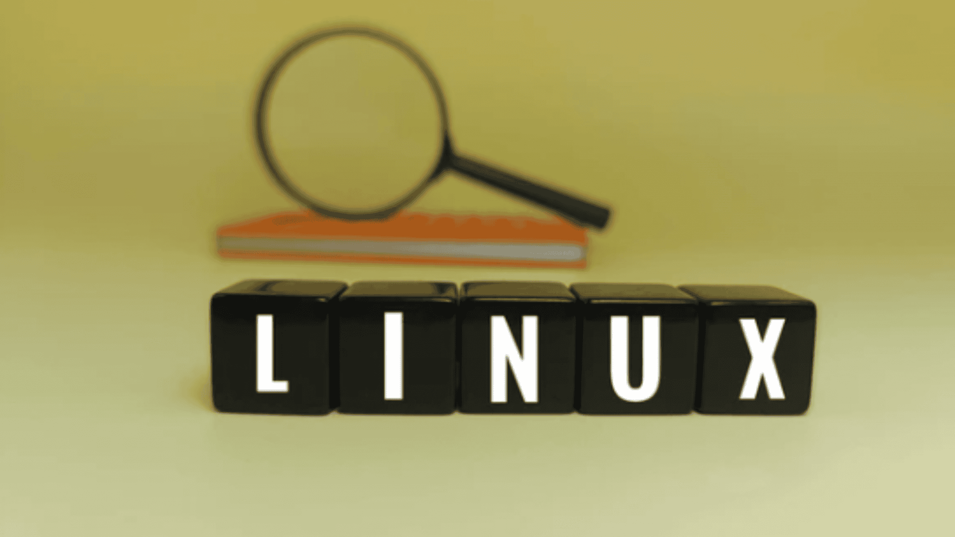 blocos pretos formando a palavra Linux em cima de uma mesa, com uma lupa no fundo