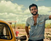 Wagner Moura encostado em uma parede ao lado de um carro