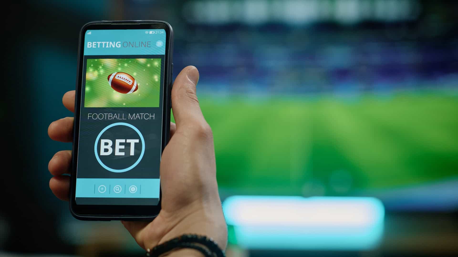 Ao fundo, borrado, uma partida de futebol passando em uma TV; à frente, a foto de uma bola de futebol americano e a palavra 