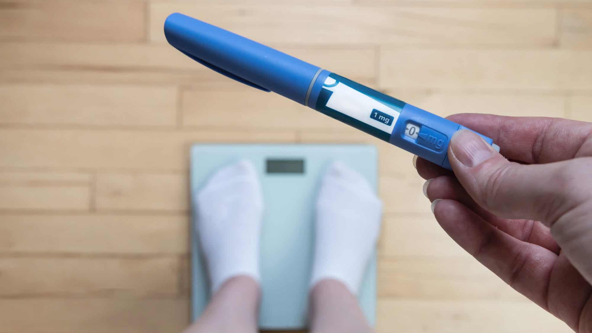 Pessoa em cima de balança de pesar segurando caneta emagrecedora