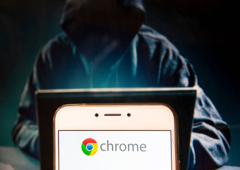 O navegador do Chrome, desenvolvido pelo Google, tem seu logotipo exibido em um dispositivo móvel Android com a figura de um hacker ao fundo