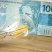 Ao fundo, uma nota de R$ 100; à frente, uma lâmpada