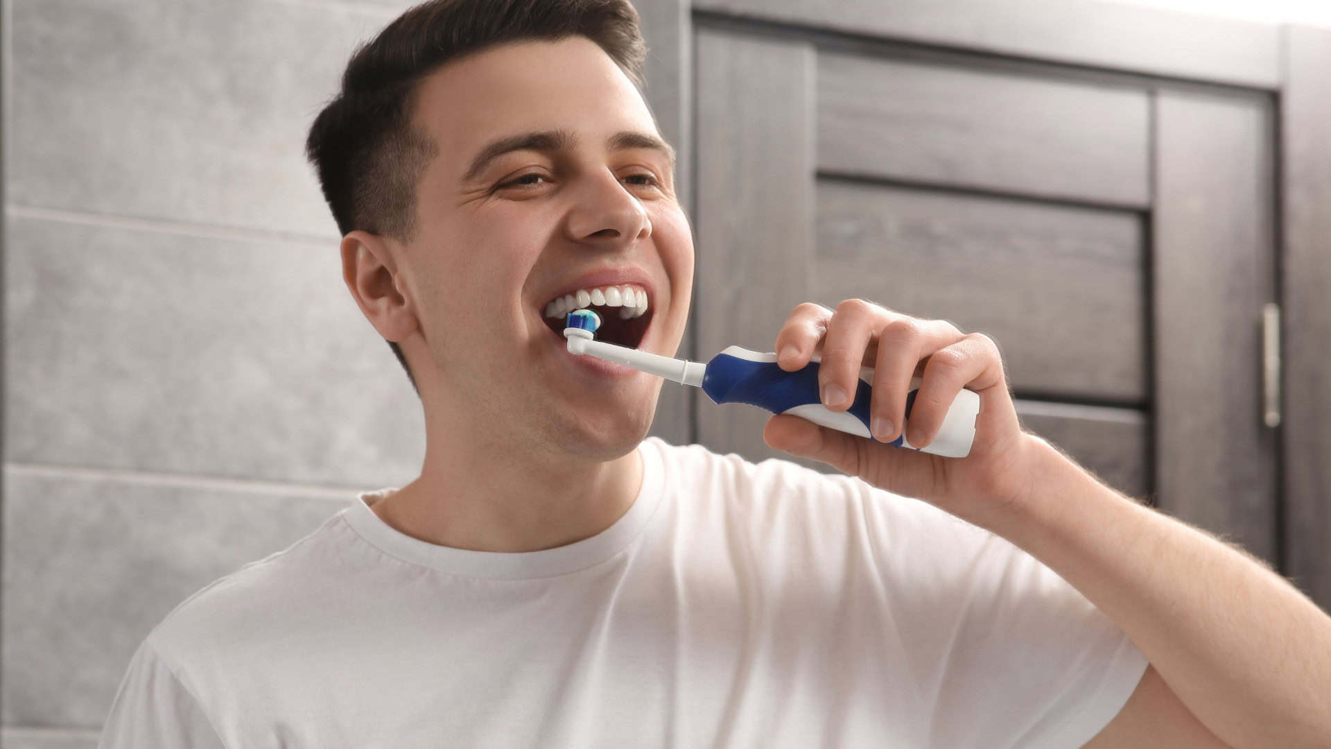 Homem escovando os dentes com escova elétrica no banheiro