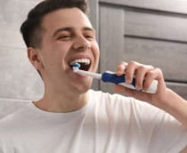 Homem escovando os dentes com escova elétrica no banheiro