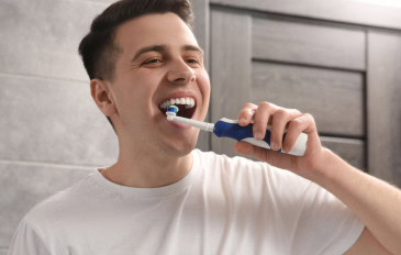 Homem escovando os dentes com escova elétrica no banheiro