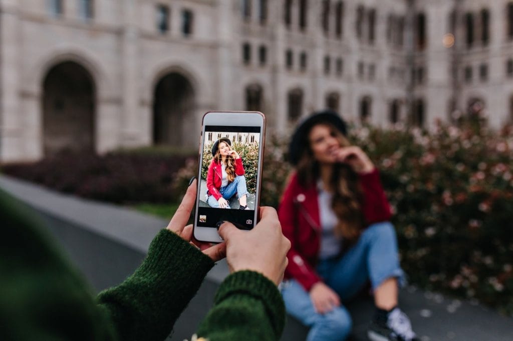Por que fotos e vídeos perdem qualidade no Instagram? Você já passou pela frustração de tirar uma foto incrível ou gravar um vídeo em 4K, ver que o arquivo está cristalino na galeria do celular, mas, ao subir para o Instagram, o resultado parece uma imagem pixelada e de qualidade inferior? Mulher tirando foto de amiga sentada ao lado