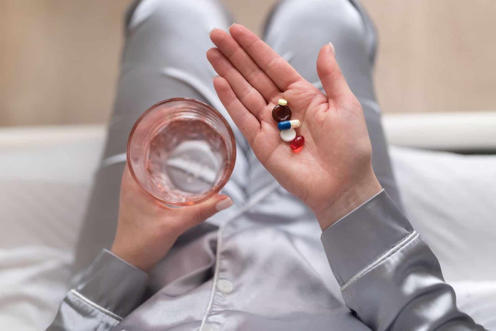 Mãos segurando um copo de água e comprimidos 