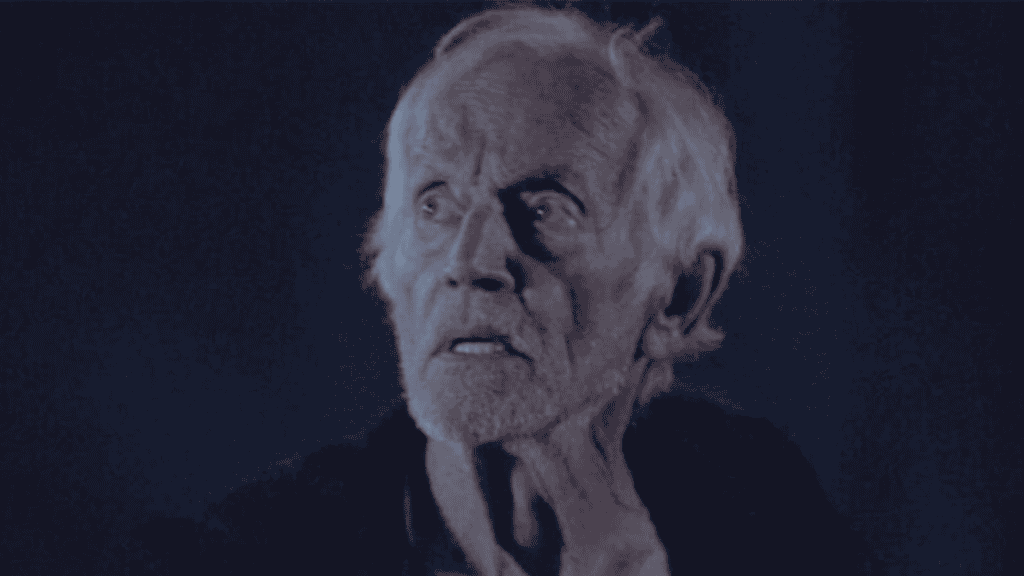 Lance Henriksen em ambiente escuro, com expressão assustada e olhar voltado para cima, em referência ao tema “atores que mais morreram em filmes e séries”